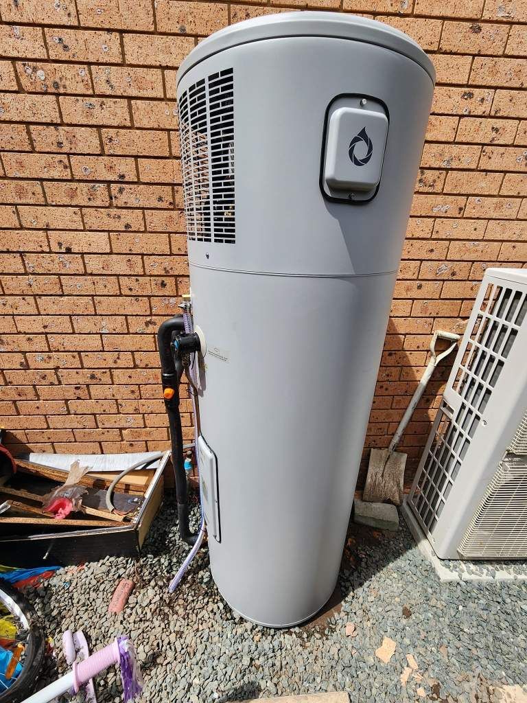 A White Water Heater Is Sitting In Front Of A Brick Wall — RAW Plumbing & Gasfitting In Pearce, ACT