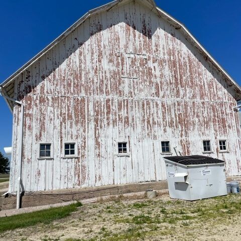 Weathered white barn with peeling paint and a dumpster in front on a sunny day