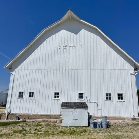 White barn exterior with small windows, a trash bin, and buckets in front under a blue sky