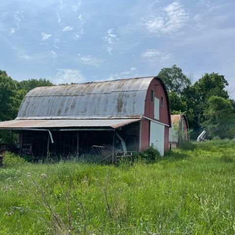 Old red barn with a curved metal roof in a grassy field under a cloudy sky