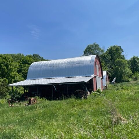 Red barn with metal roof in a grassy field under a clear blue sky