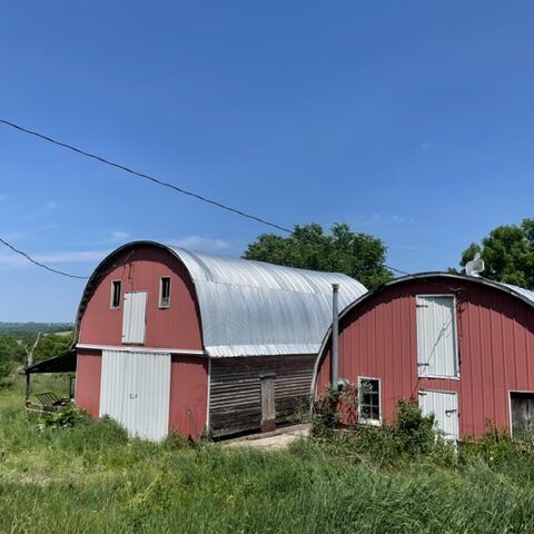 Two red barn sheds with silver curved roofs in a grassy rural field under a blue sky
