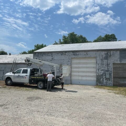 Utility truck with bucket lift parked beside a gray warehouse, with two workers standing nearby.