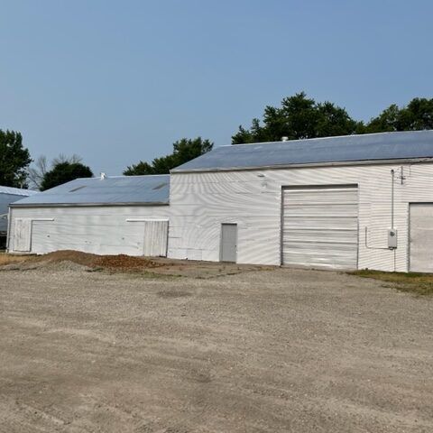 White metal warehouse buildings with large garage doors beside a gravel lot under a clear blue sky