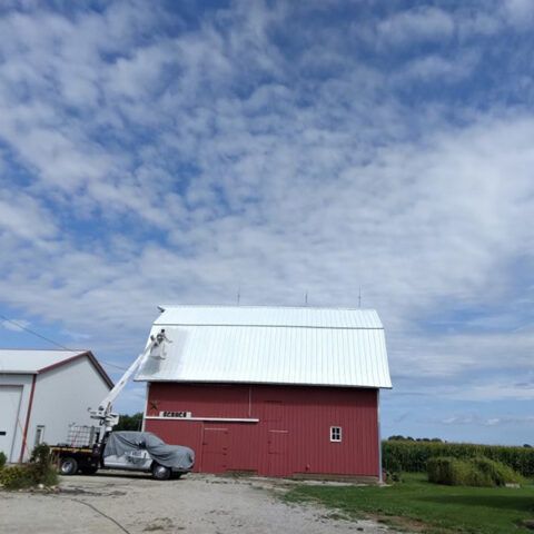 Red barn with white roof under a cloudy blue sky, next to a parked car and grassy field