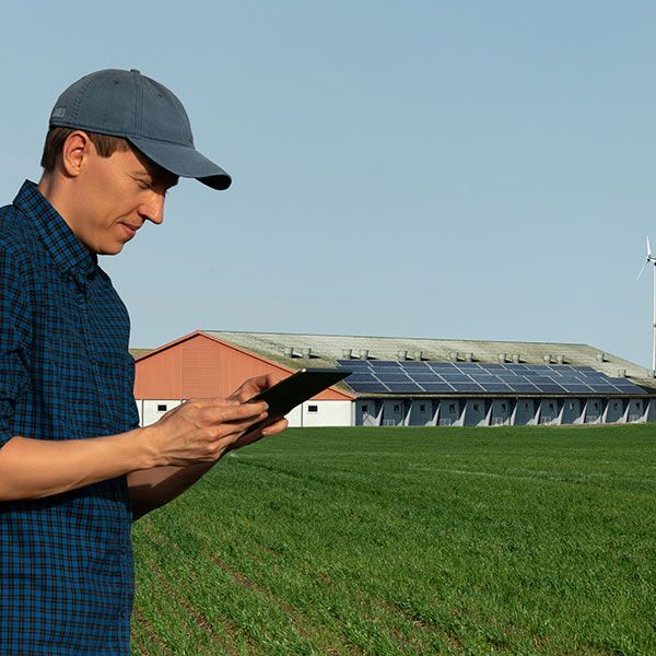 Man in a blue cap using a tablet beside a grassy field and stadium building