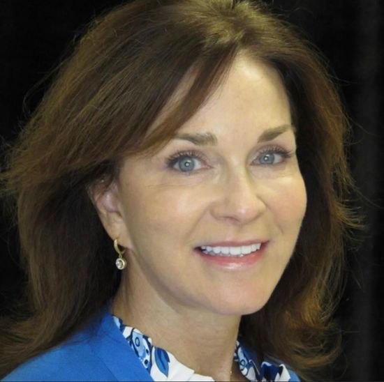 A woman wearing a blue shirt and earrings smiles for the camera