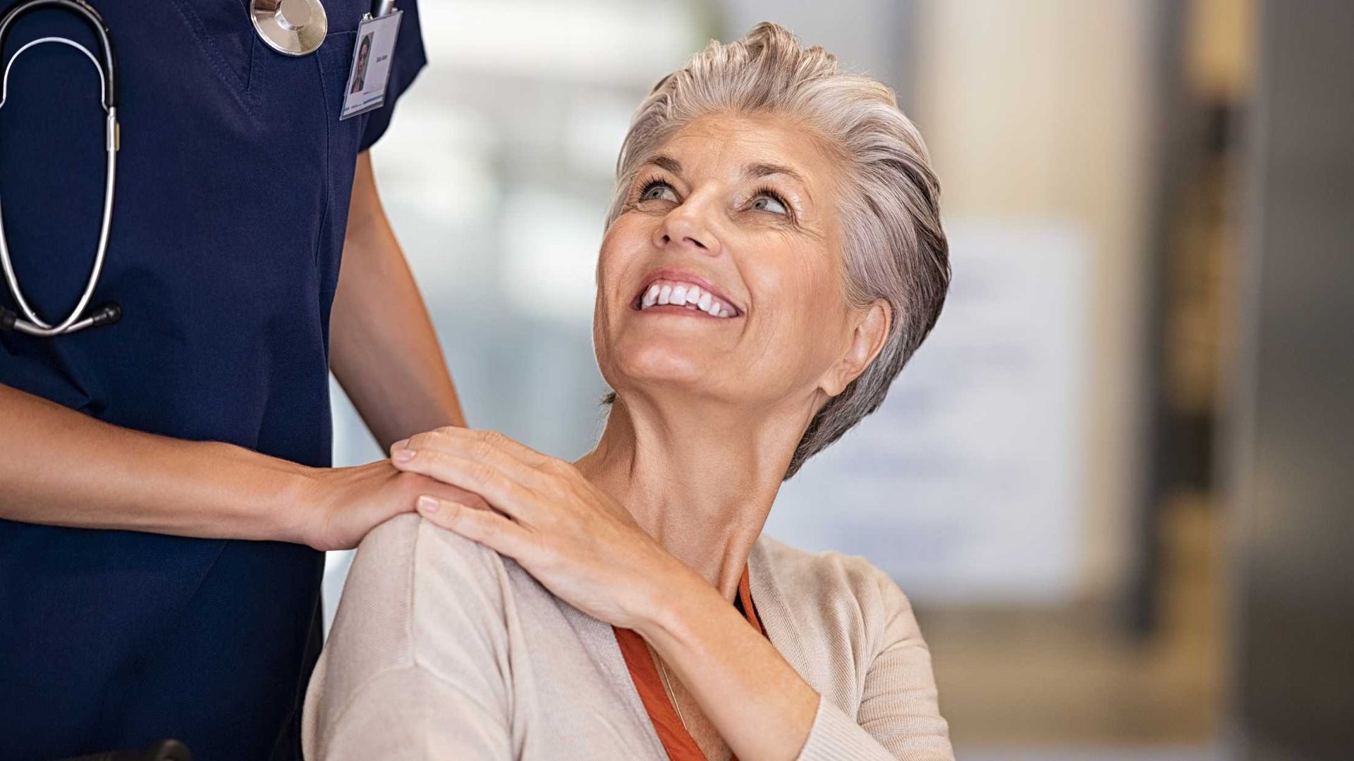 An elderly woman in a wheelchair is being comforted by a nurse.