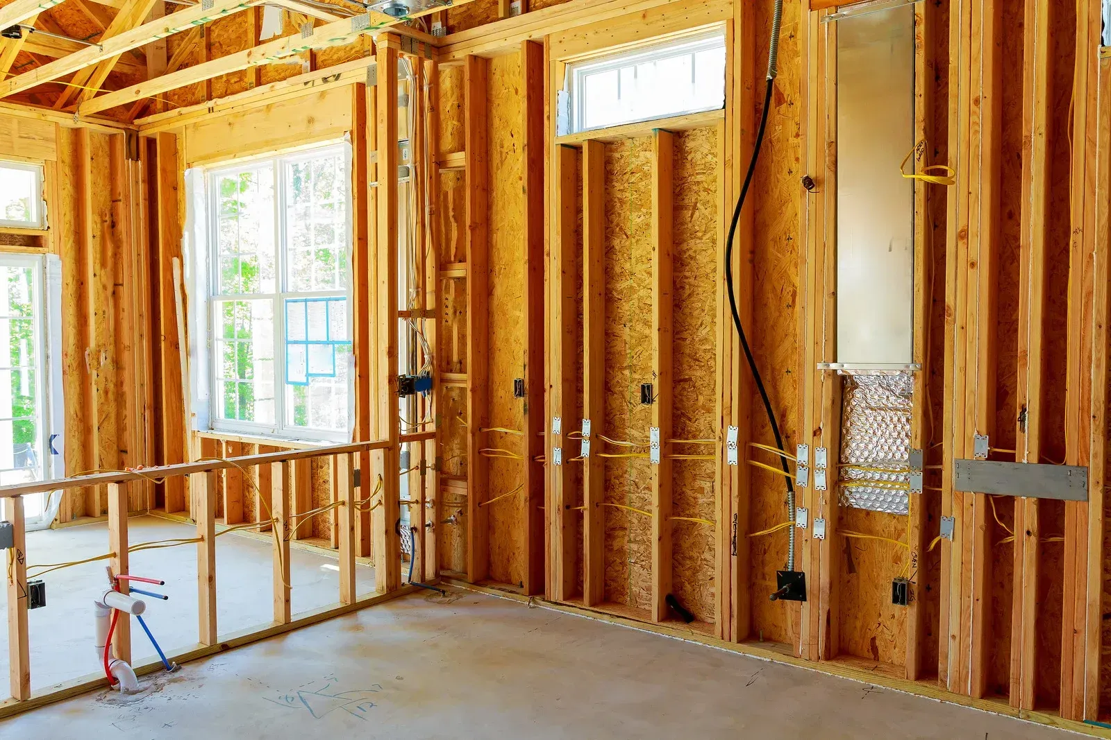 Partially framed interior with exposed wooden studs, windows, and a concrete floor during construction