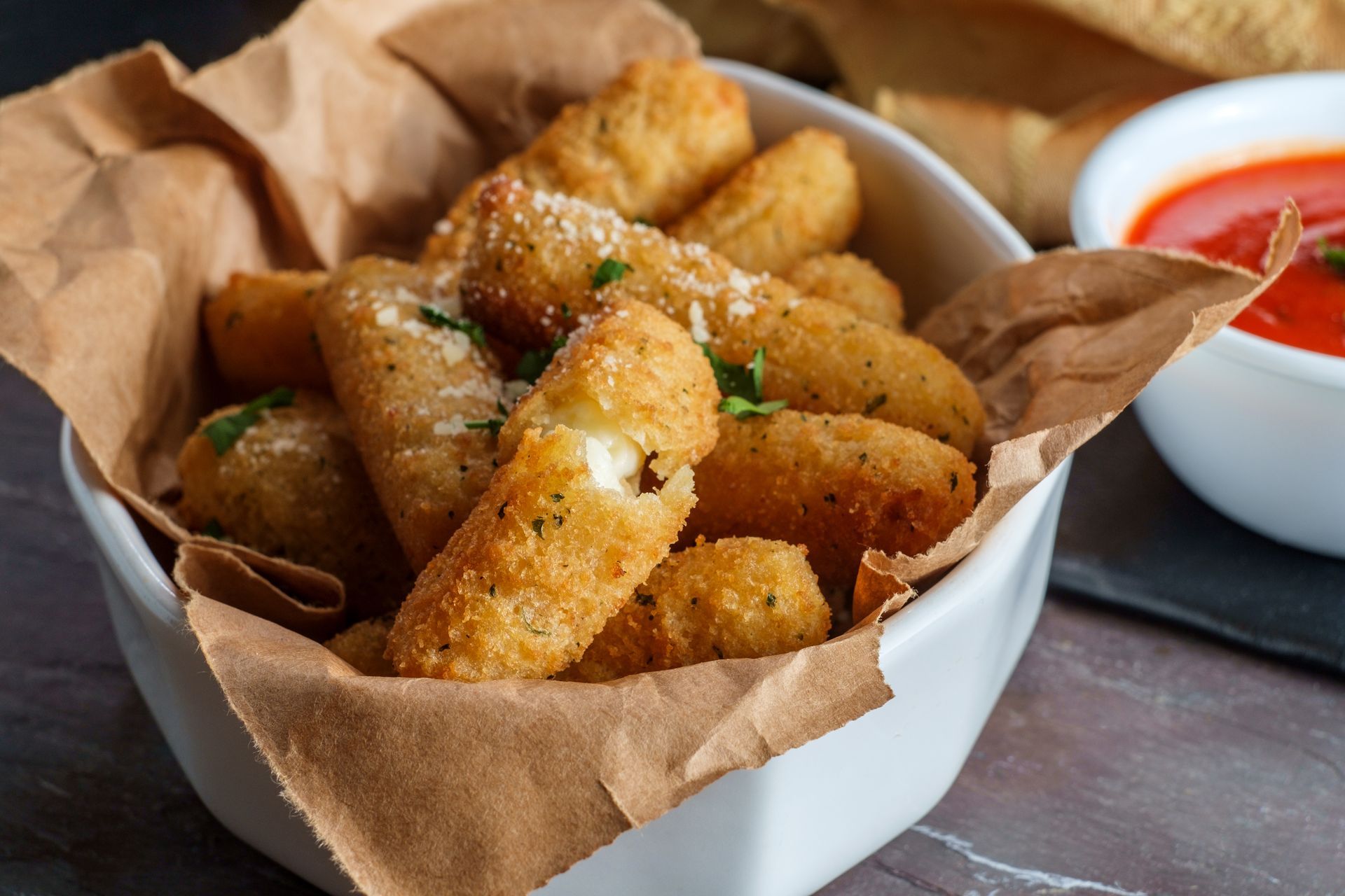 Basket of golden fried cheese sticks with dipping sauce on a table
