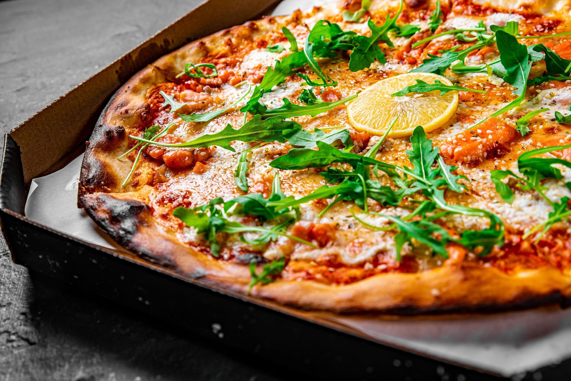 Pizza with greens and lemon on a dark tray