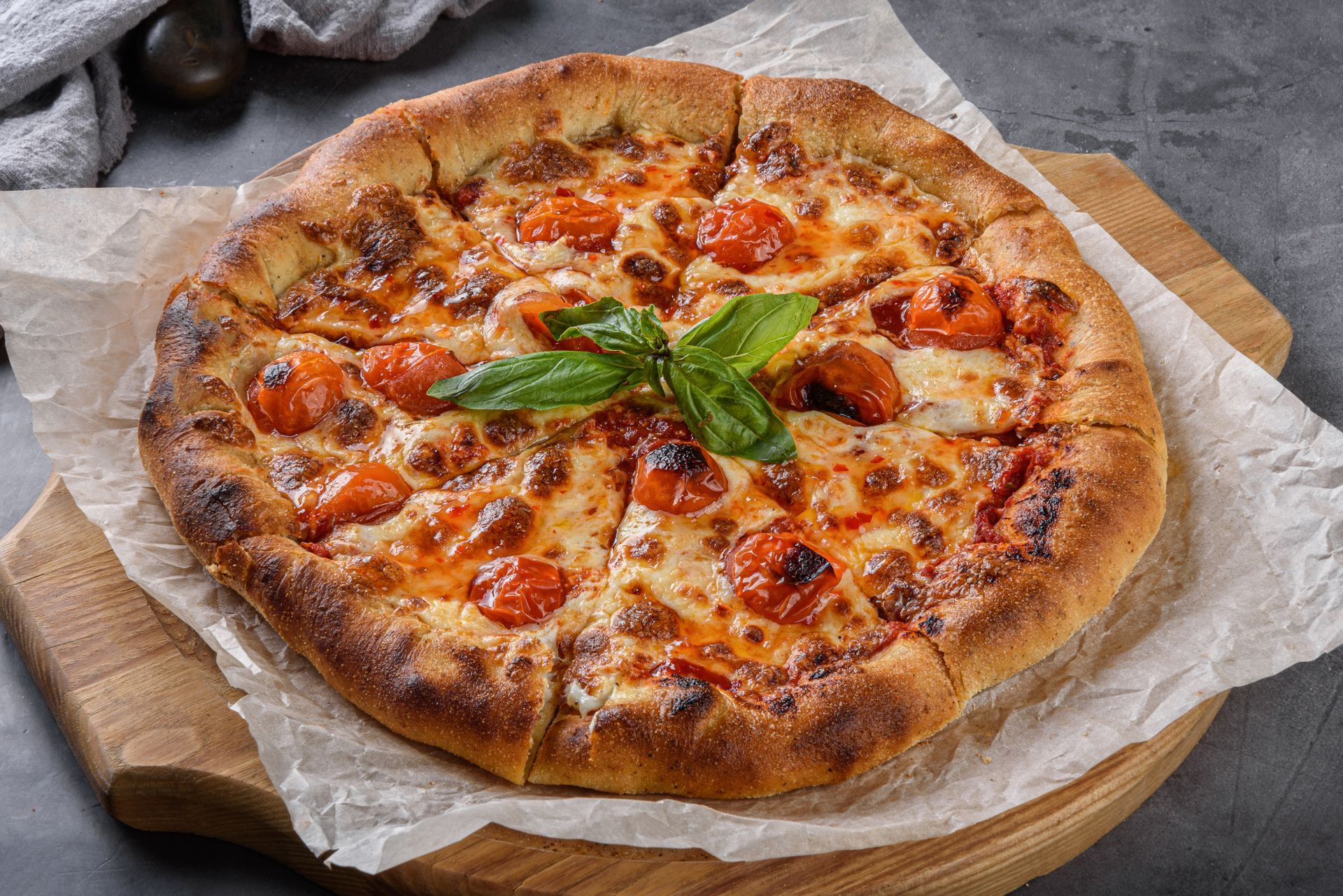Wood-fired pizza with melted cheese, tomato sauce, and basil on parchment paper on a wooden board