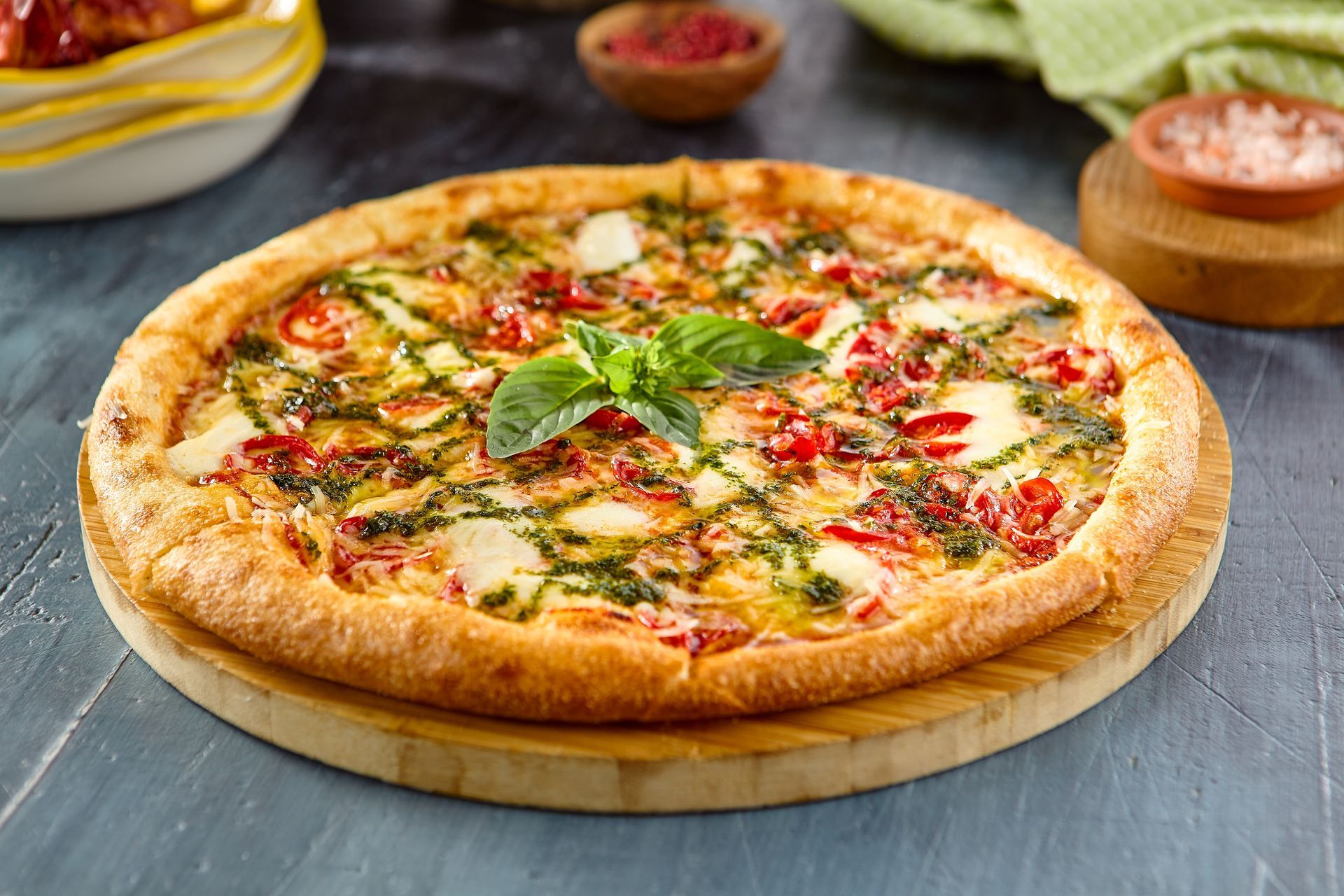 Cheese and herb pizza on a wooden board with bowls of sauce in the background
