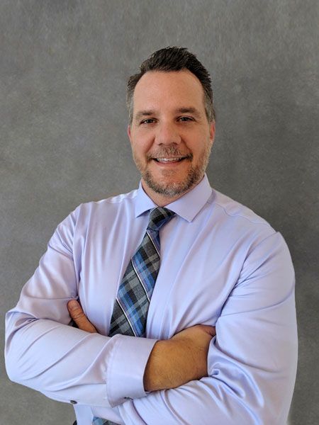 a man in a purple shirt and plaid tie is standing with his arms crossed .