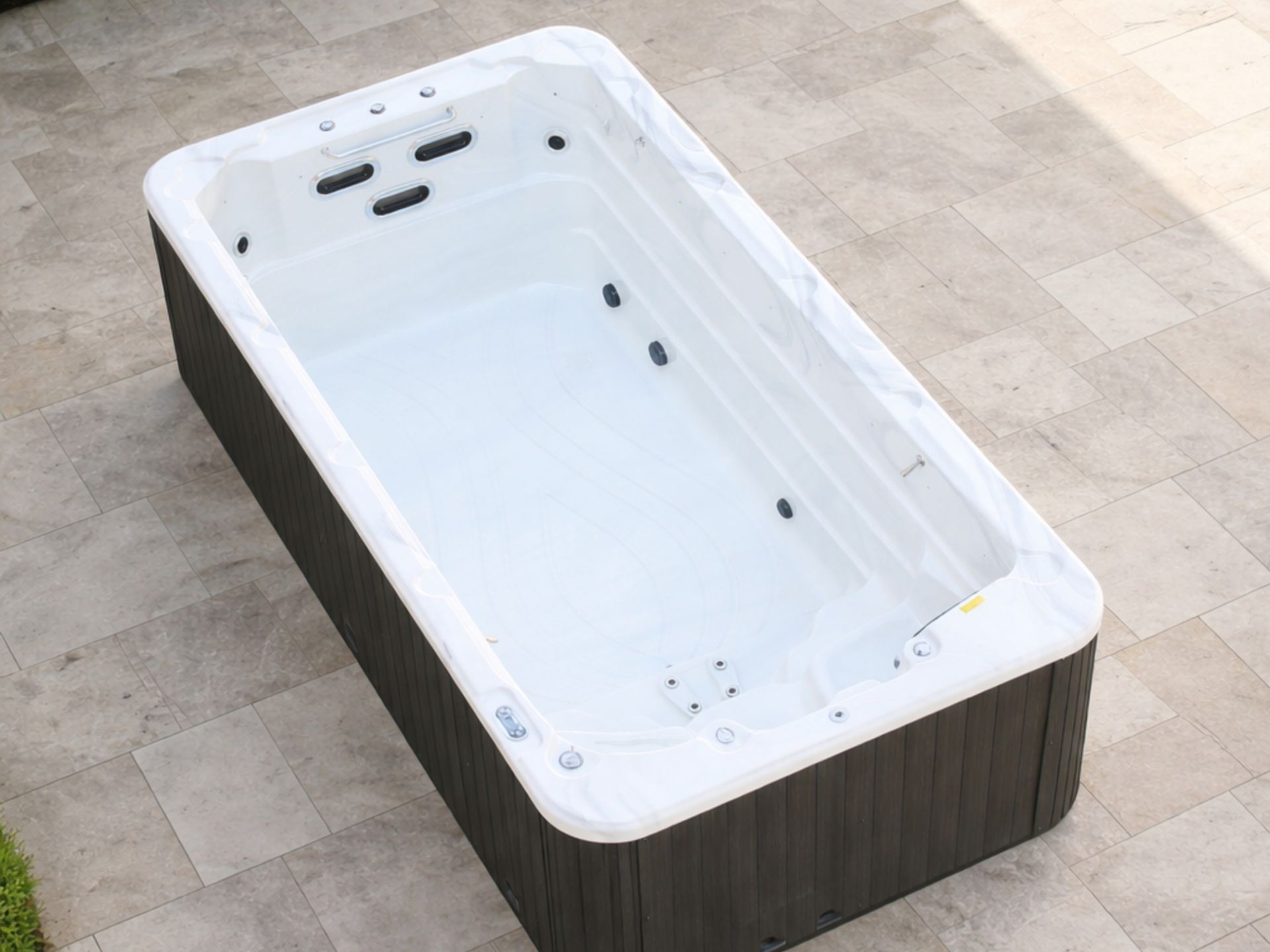 Top view of an above-ground swim spa with a white acrylic interior, integrated counter current swim jets, and spa massage jets, designed for home fitness, relaxation, and small outdoor spaces.
