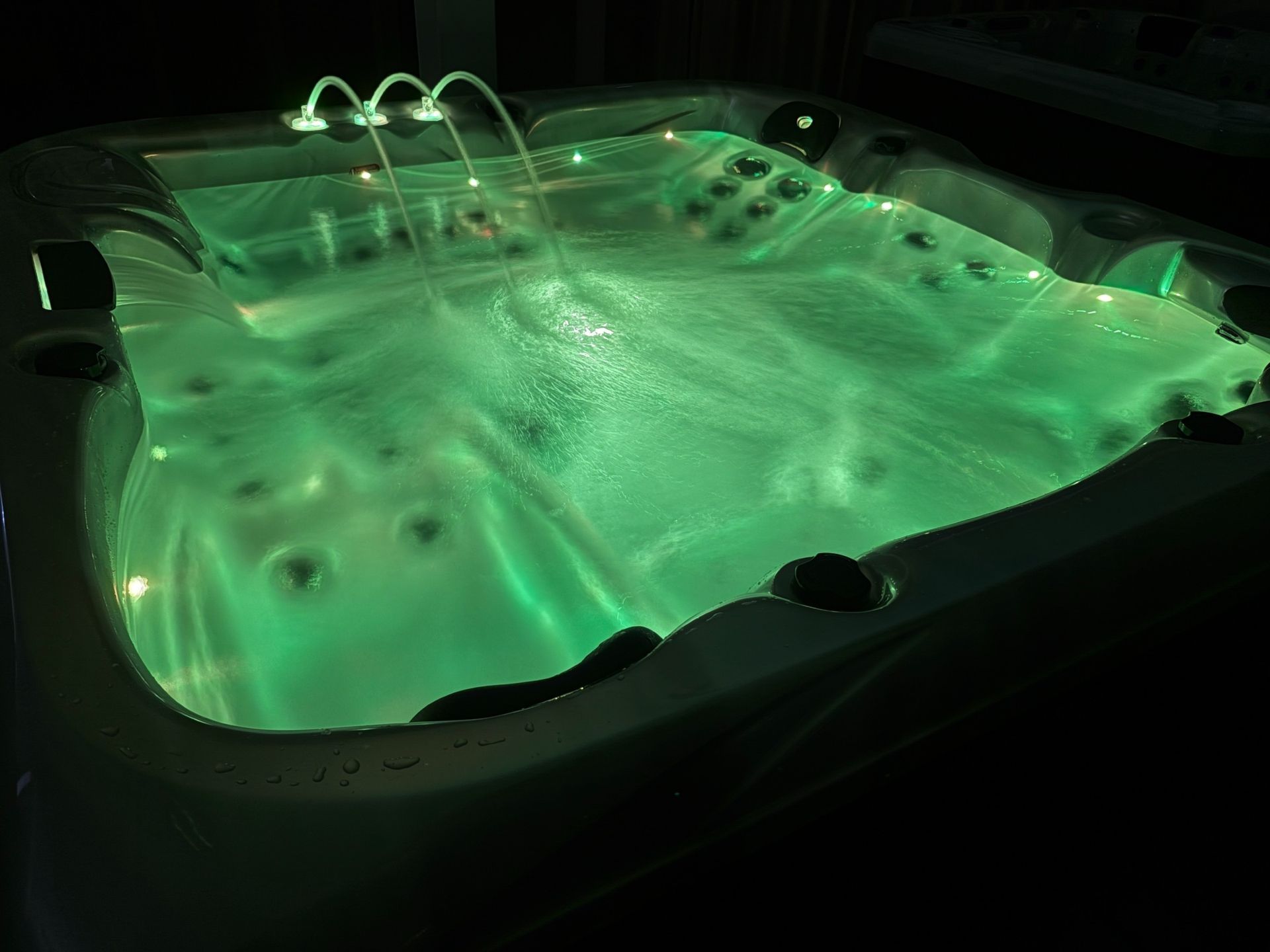 Q&G outdoor hot tub at night with green LED lighting and water fountains spraying into the warm water