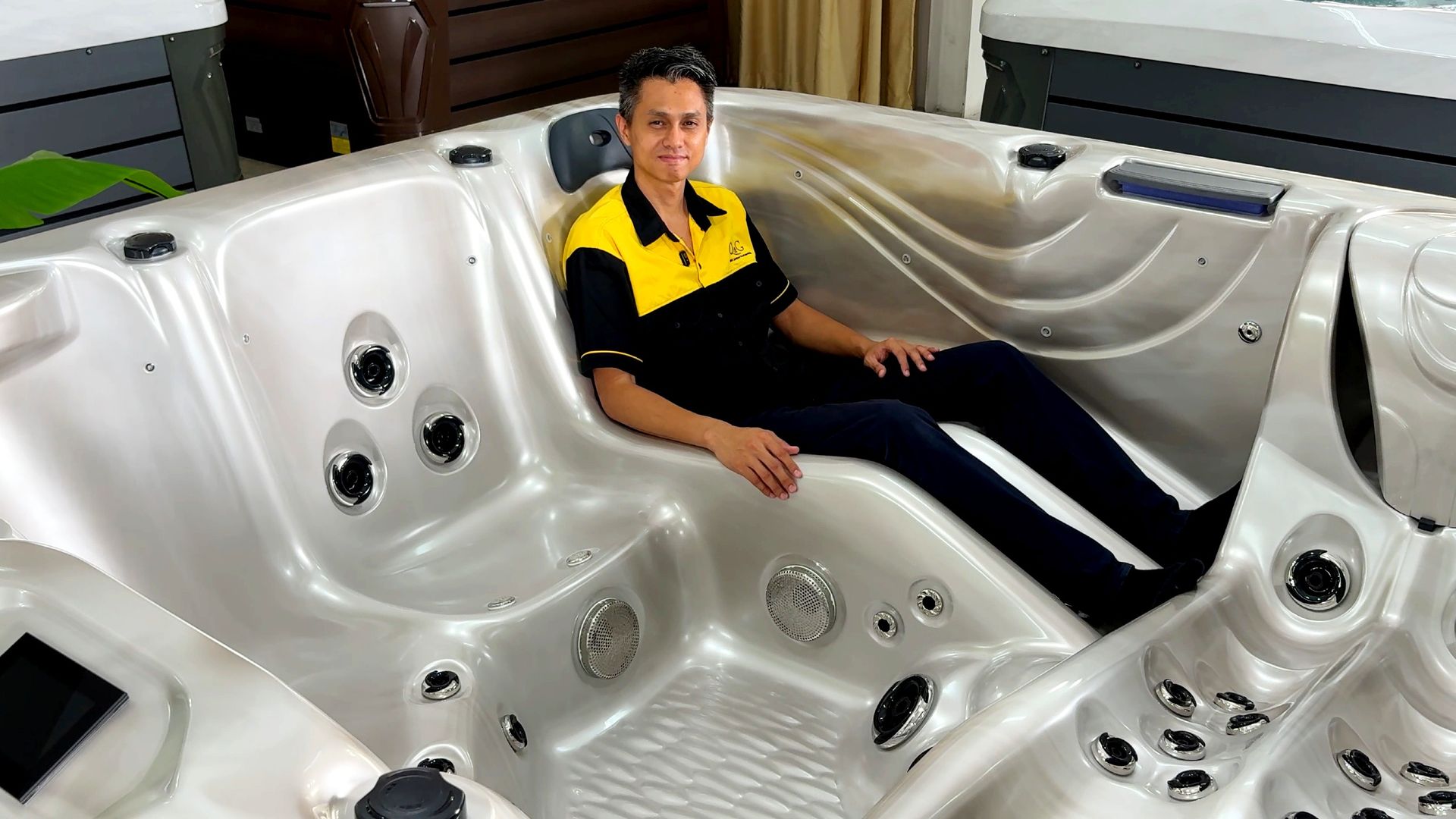 ภาพอ่างน้ำร้อนภายนอกบ้าน ดีไซน์ที่นั่งแบบเอนนอน (Lounger Seat) พร้อมระบบเจ็ทนวดหลายจุดบริเวณหลัง เอว และขา มีนายแบบนั่งสาธิตขนาดที่นั่งภายในอ่าง แสดงพื้นที่ใช้งานจริง เหมาะสำหรับติดตั้งในบ้านพักอาศัยและรีสอร์ตในประเทศไทย