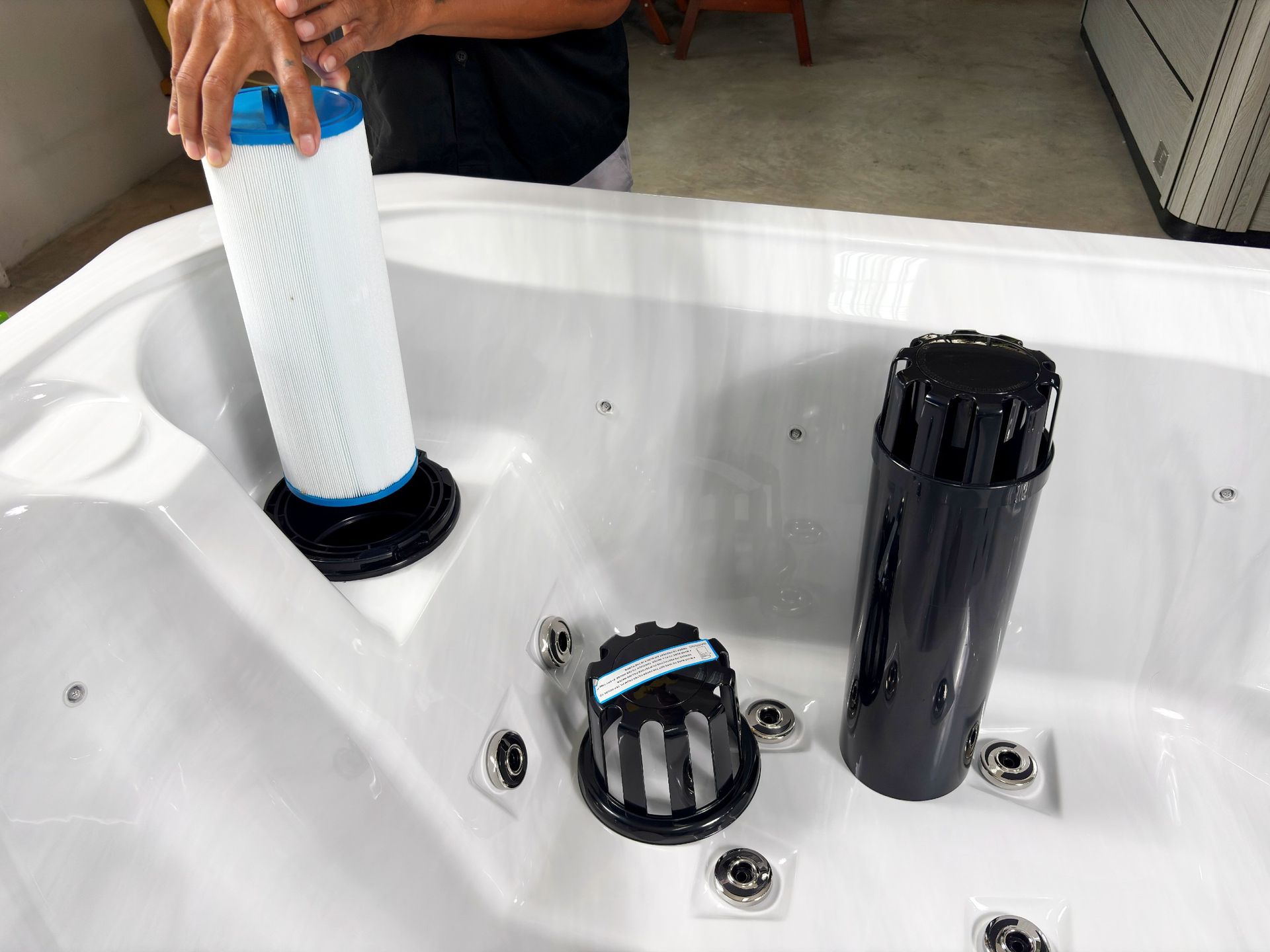 ภาพการถอดไส้กรอง (Filter Cartridge) ออกจากสกิมเมอร์ของอ่างน้ำร้อนภายนอกบ้าน เพื่อทำความสะอาดและบำรุงรักษาระบบกรองน้ำ ช่วยรักษาคุณภาพน้ำให้ใสสะอาด ลดการสะสมของสิ่งสกปรก และยืดอายุการใช้งานของระบบกรอง เหมาะสำหรับการดูแลอ่างสปากลางแจ้งอย่างถูกวิธี