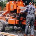 Worker operating an orange wood chipper outdoors, feeding branches into the machine.