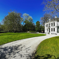Curved gravel path through a green park beside a white mansion under a bright blue sky