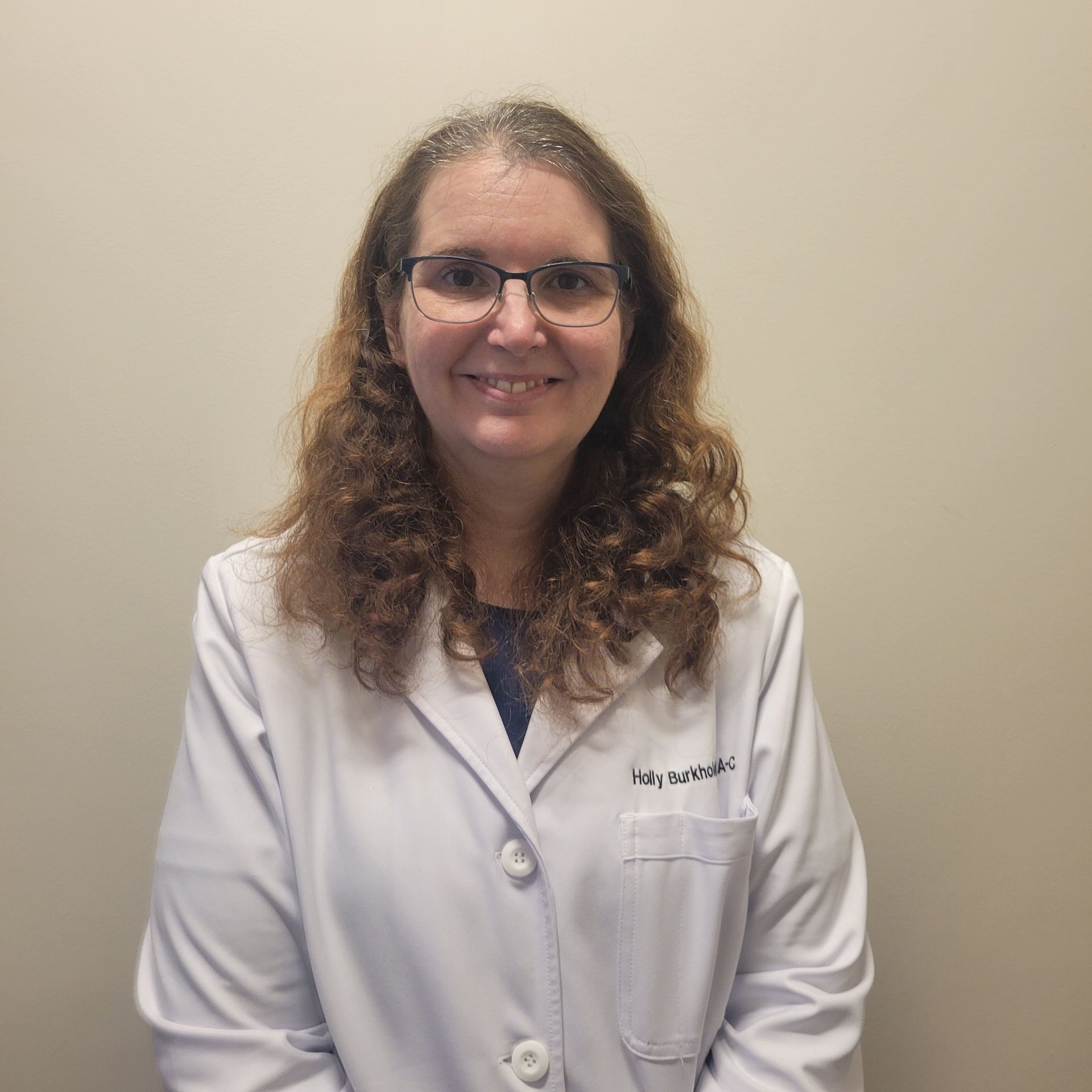 Woman in a white lab coat smiling against a plain beige background