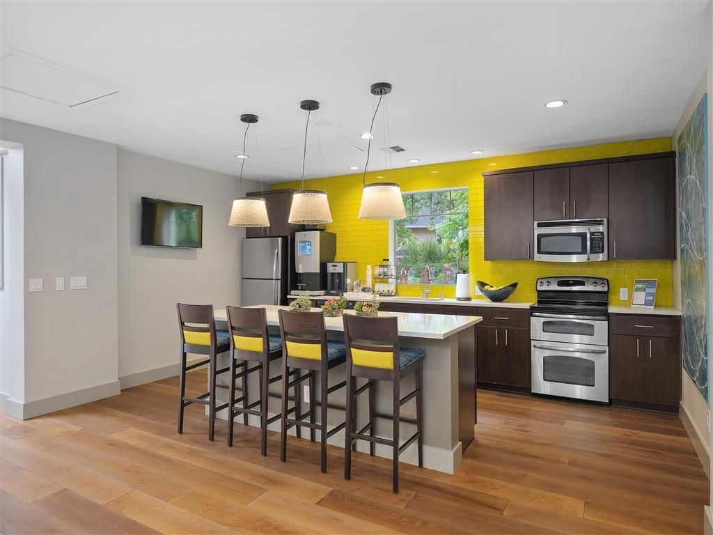 Modern kitchen with island, brown cabinets, yellow backsplash, and bar stools.