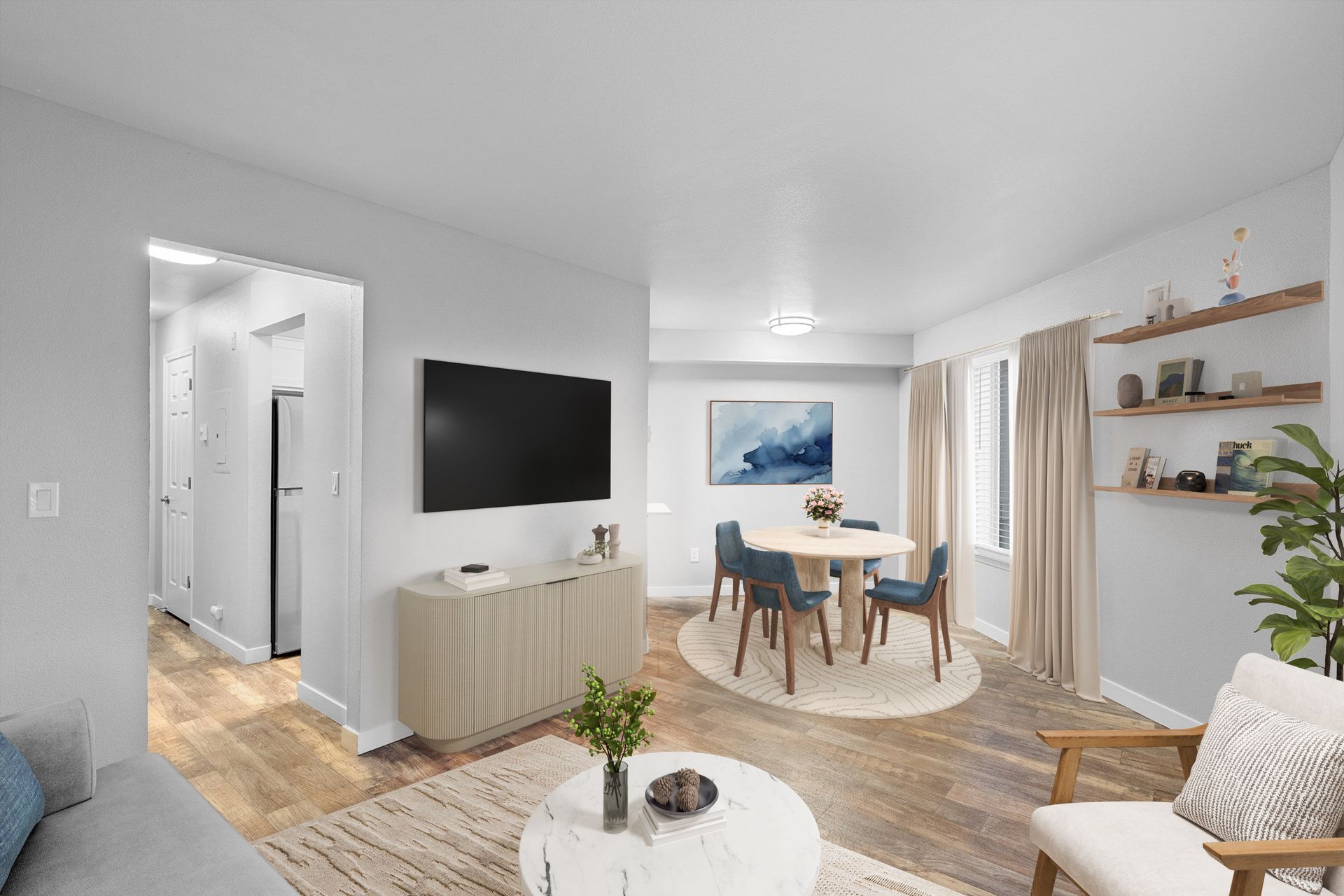 Bright living room with TV, round dining table, blue chairs, beige curtains.