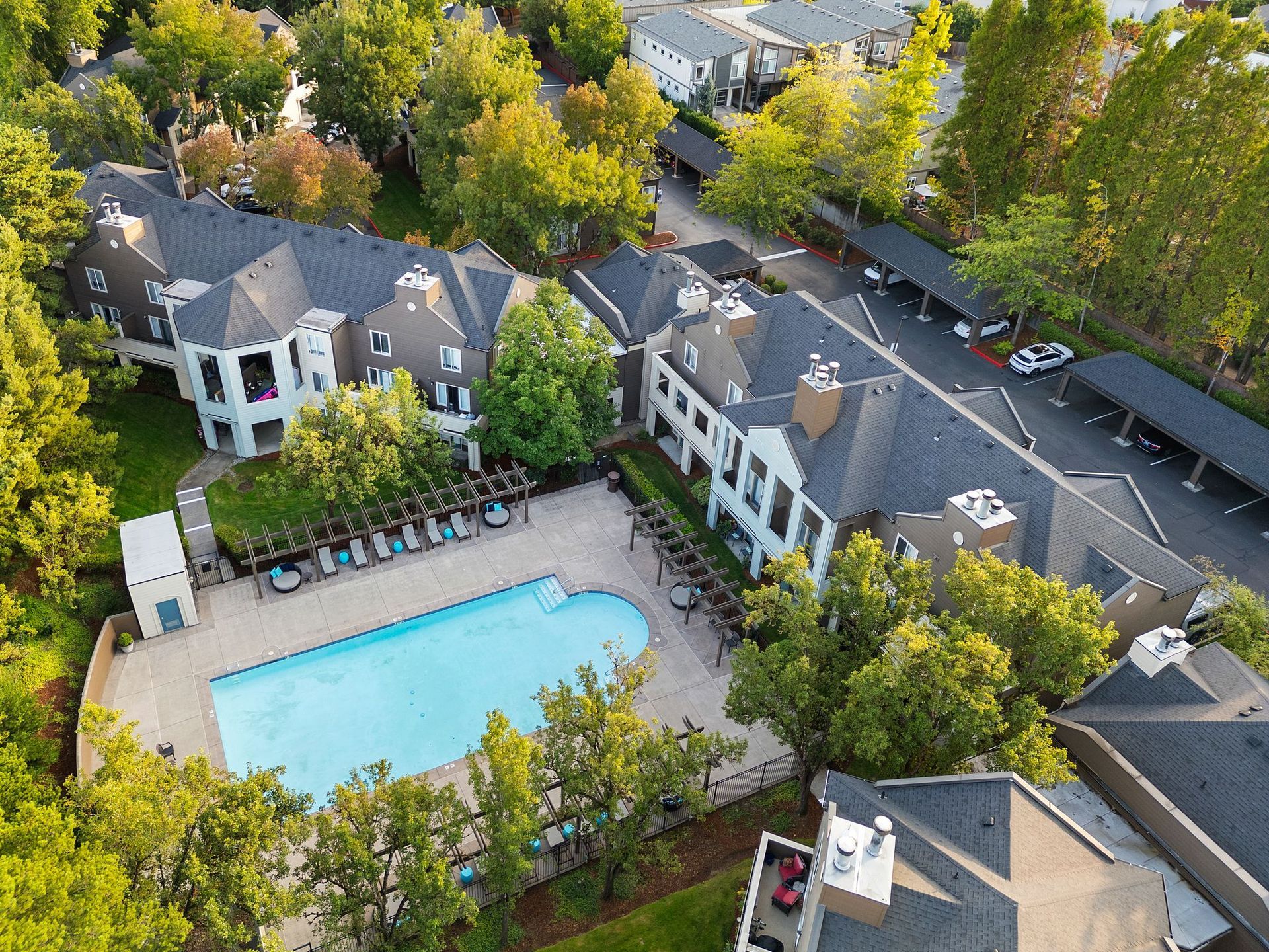 Aerial view of an apartment complex with a pool, trees, and parking structures.