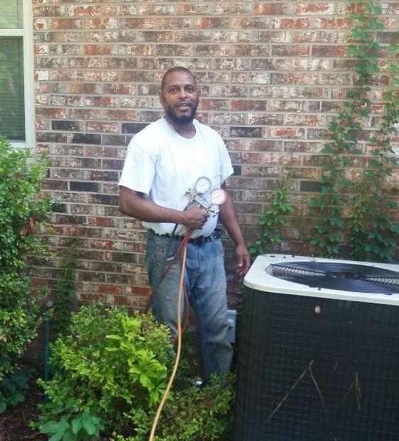 A man is standing in front of a brick building next to a propane cylinder.