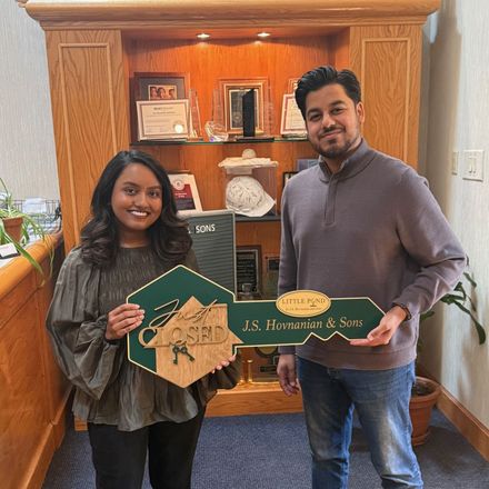 Two people holding green plaque signs in a wood-paneled office lobby