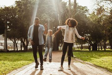 Three people walking and jumping on a sunlit park path with trees in the background.