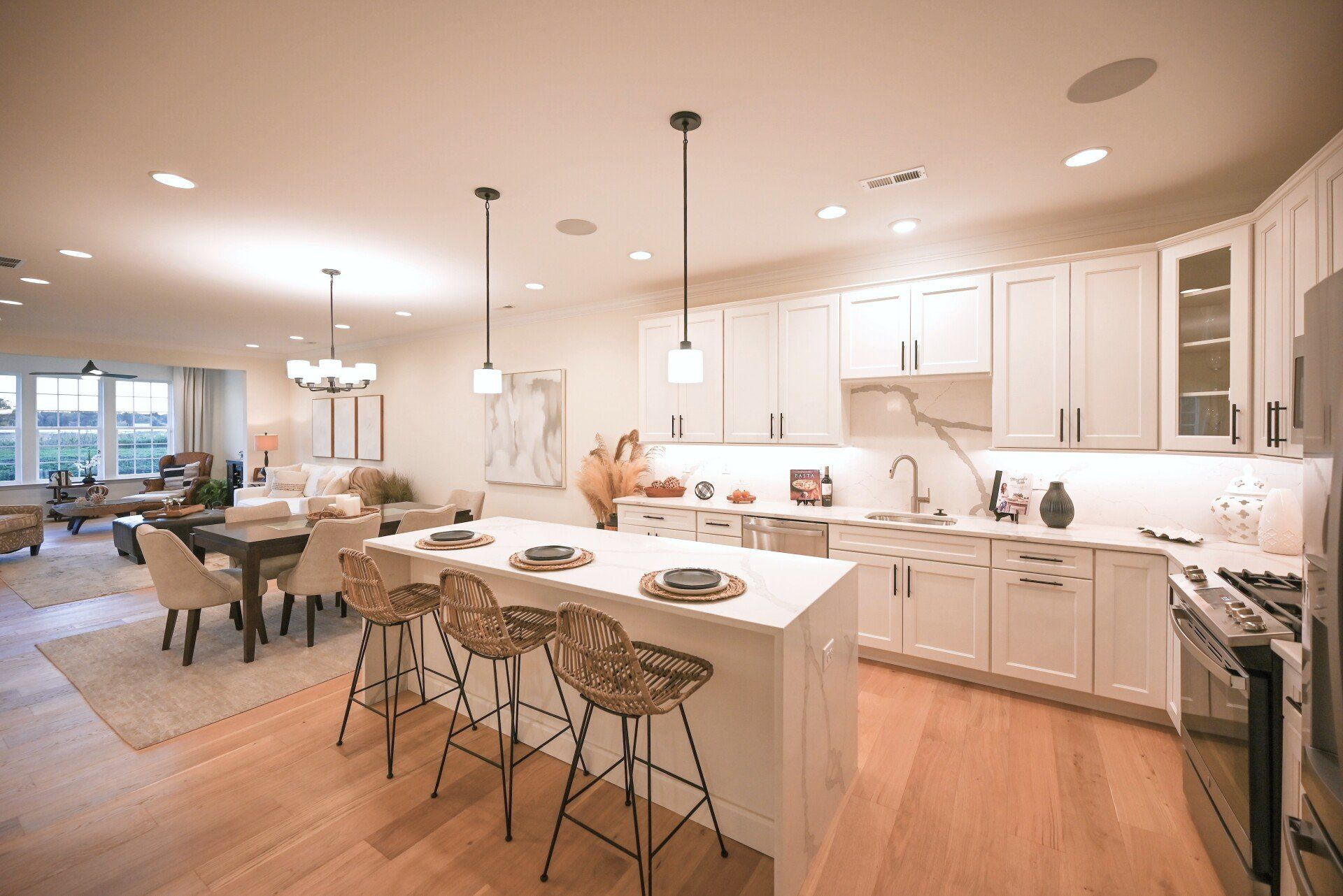 Bright modern kitchen with white cabinets, island seating, and open dining area overlooking a living room