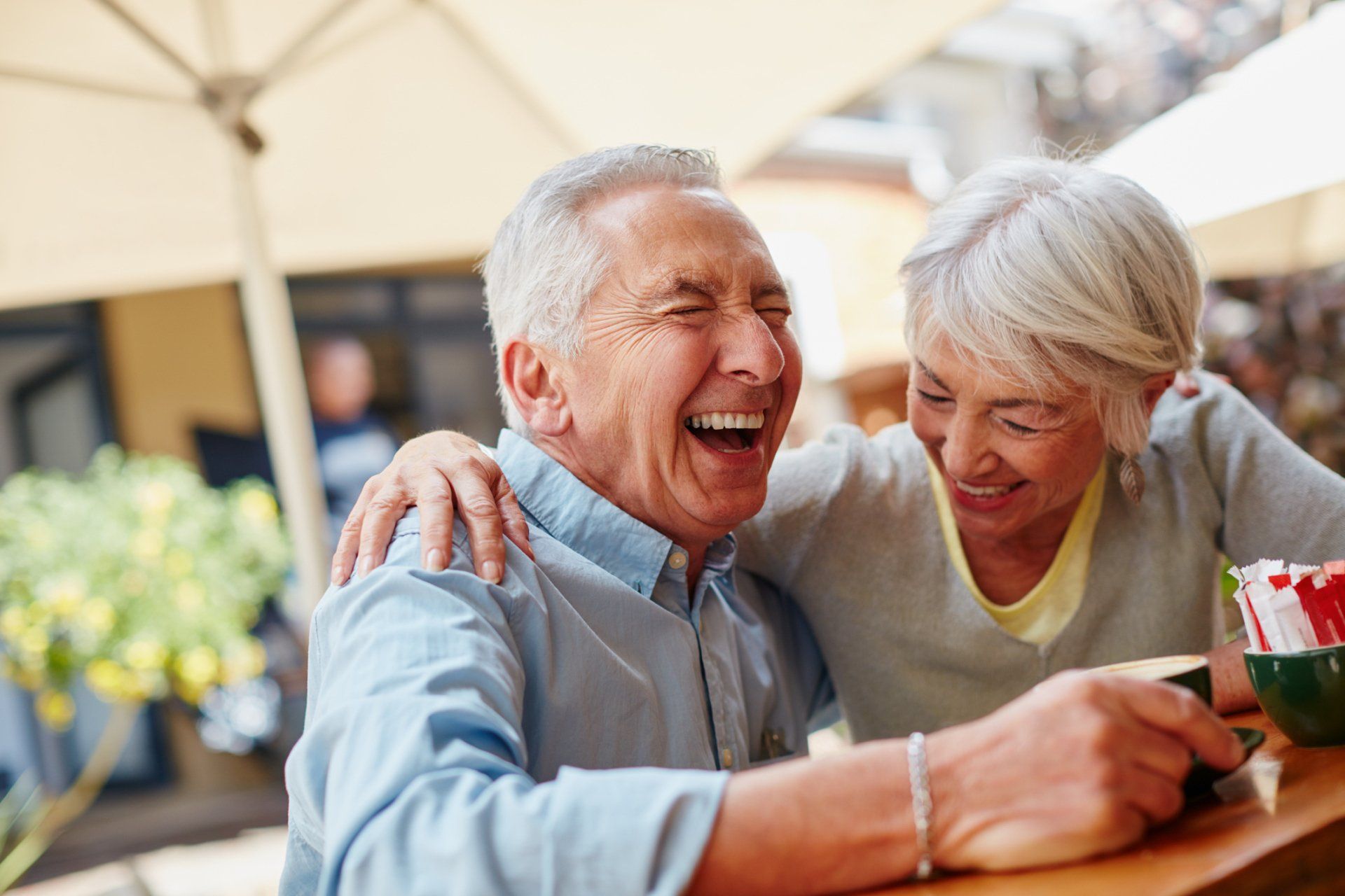 Two people laughing together at an outdoor café table, sharing a relaxed moment