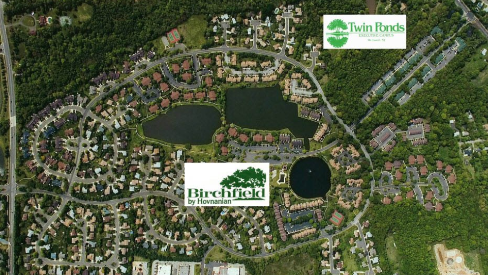 Aerial view of a suburban neighborhood with winding streets, ponds, and wooded green spaces.