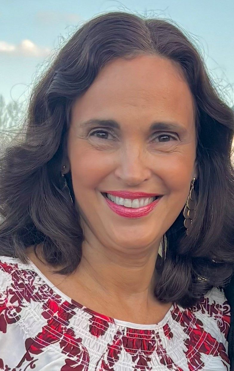 Smiling woman with shoulder-length white hair wearing a turquoise knit top and pearl necklace