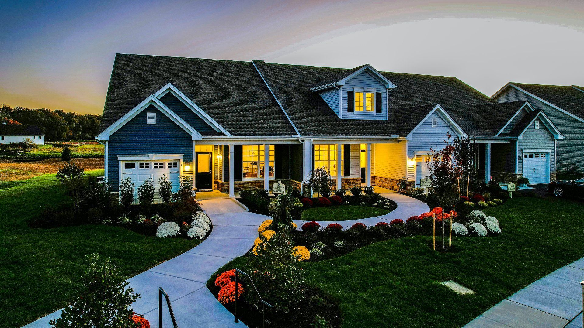 Suburban house at dusk with lit windows, curved walkway, and landscaped front yard