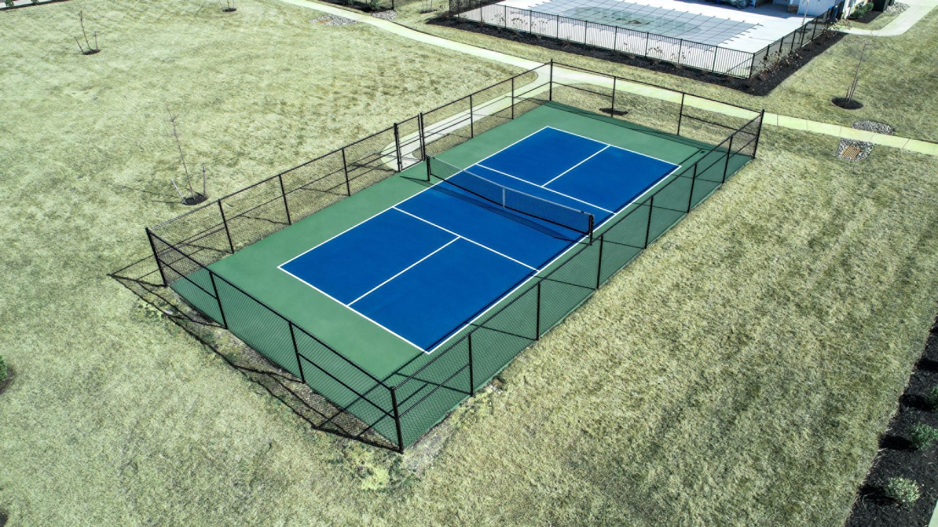 Outdoor blue pickleball court enclosed by a black fence on a grassy field