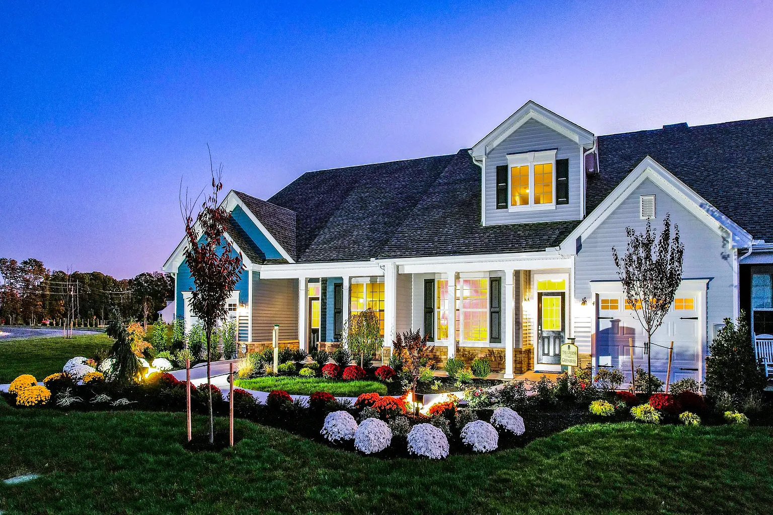 A charming house with lit windows and a flower-filled garden at dusk.