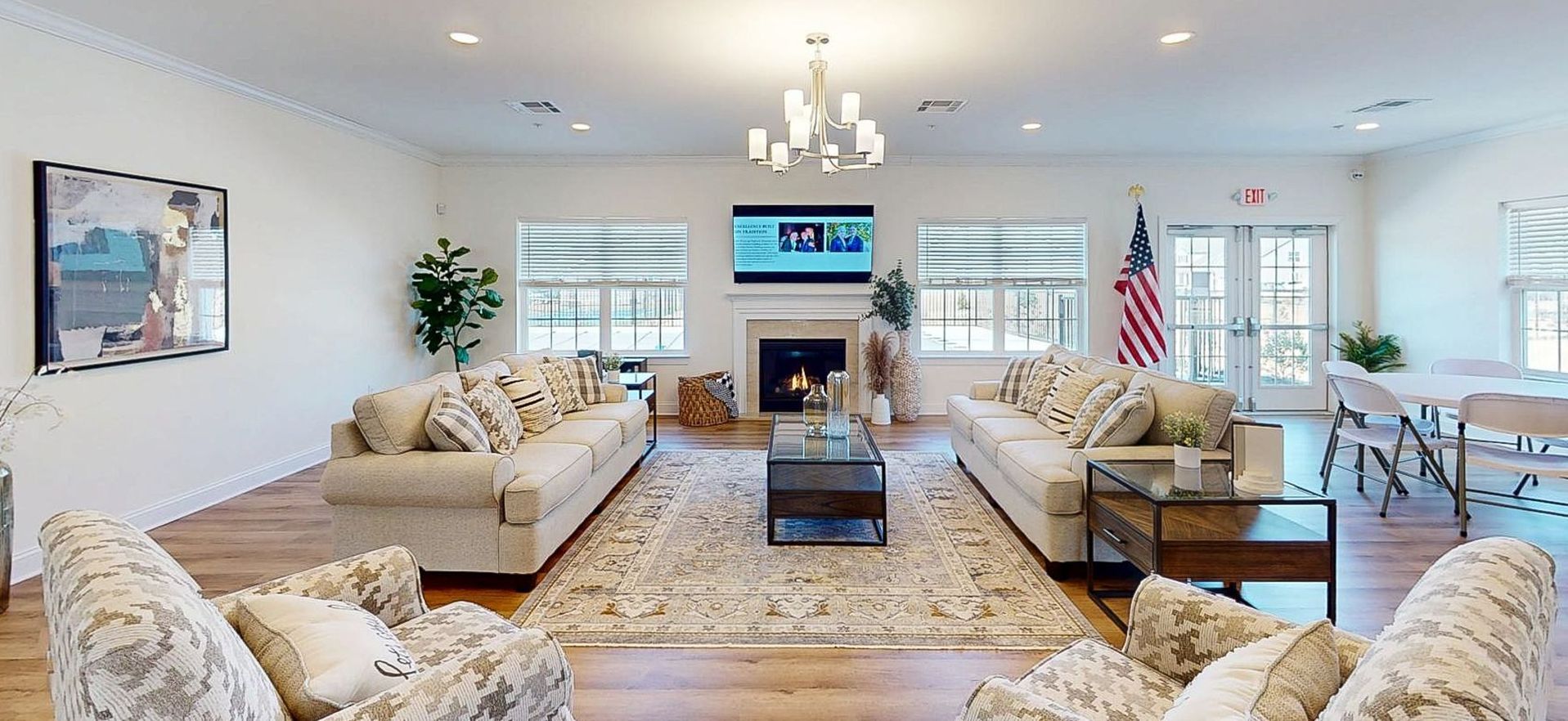 Bright living room with cream sofas, fireplace, chandelier, windows, and an American flag