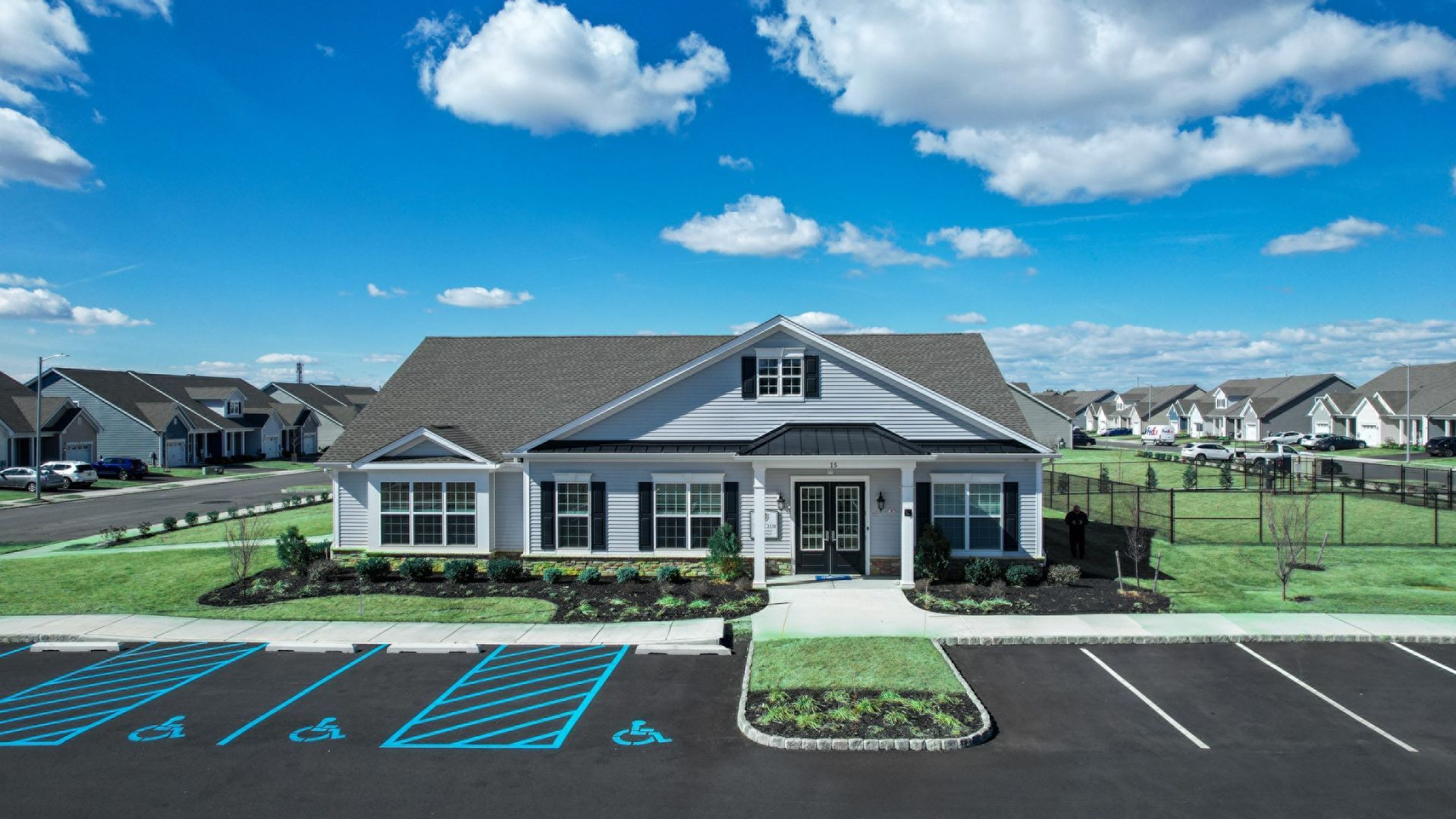 Suburban clubhouse with gray roof, blue sky, and empty accessible parking spaces in front