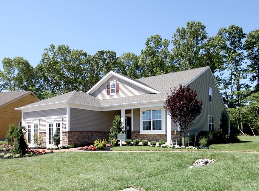 Suburban single-story house with white trim, brick accents, and a green lawn under a blue sky