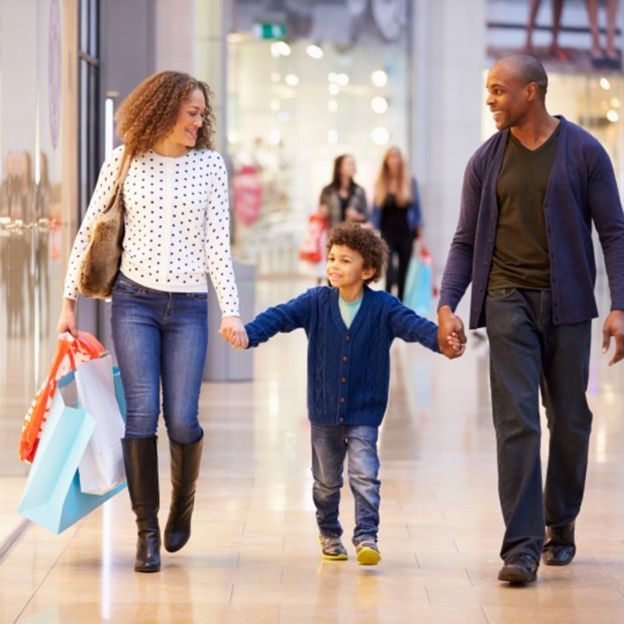 A family walking hand-in-hand through a shopping mall, carrying shopping bags.