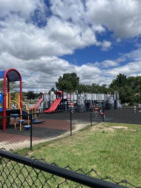 Children’s playground with slides and climbing structure behind a chain-link fence under a cloudy sky