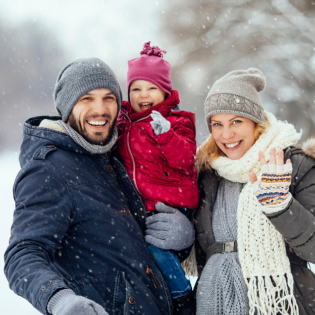 Family smiling outdoors in snowy weather, bundled in winter coats and hats.