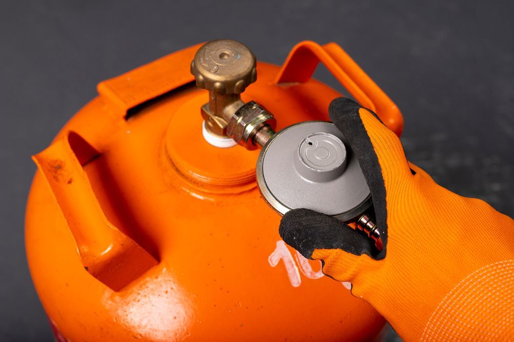 Orange Gloved Hand Using a Grey Regulator on An Orange Gas Cylinder — Kuranda Gas & Supplies In Port Douglas, QLD