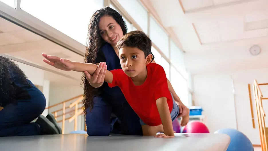a woman is helping a young boy crawl on the floor in a gym .