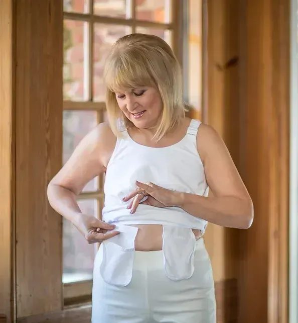 a woman in a white tank top and white pants is standing in front of a window .