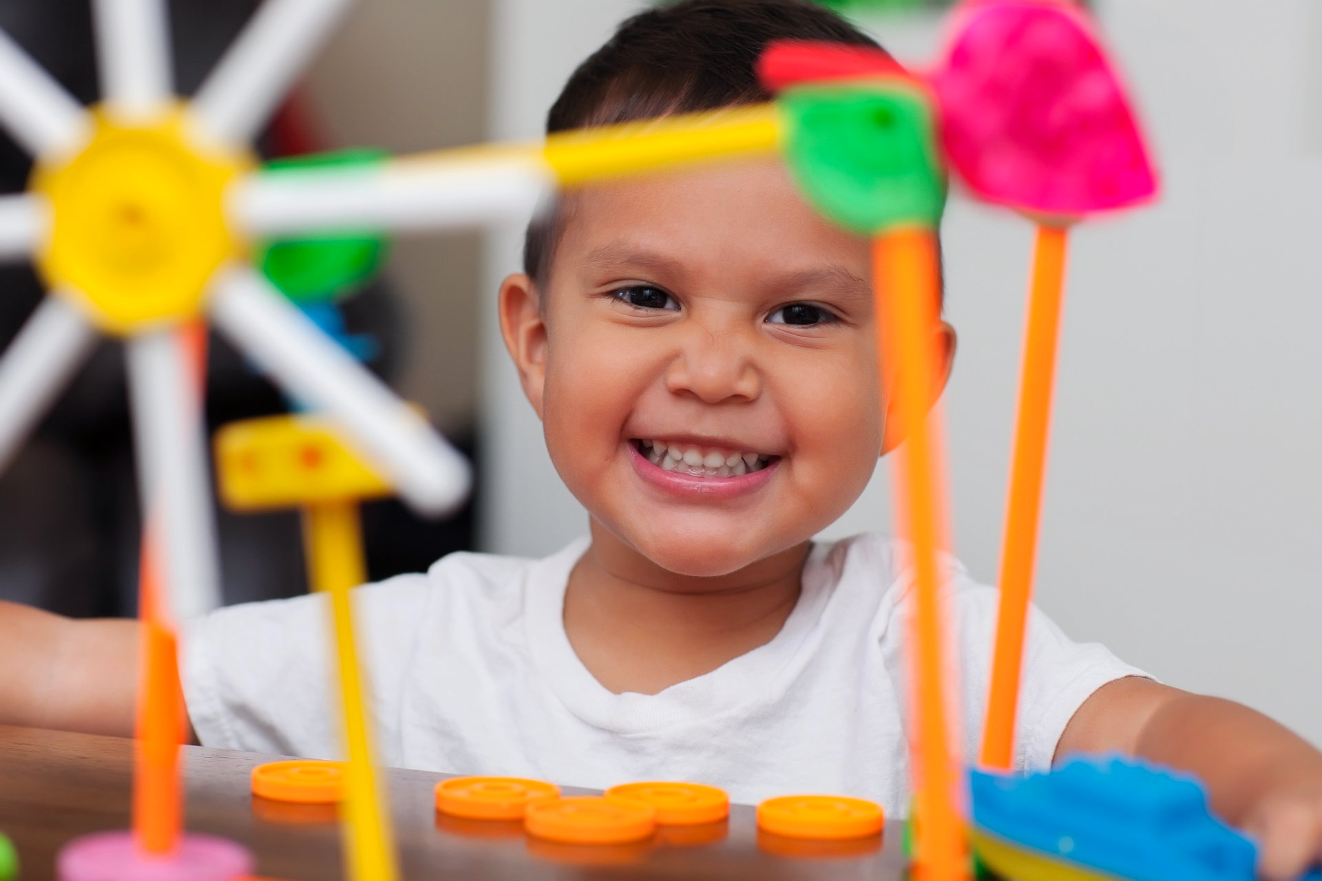 A young boy is smiling while playing with a colorful toy ferris wheel.