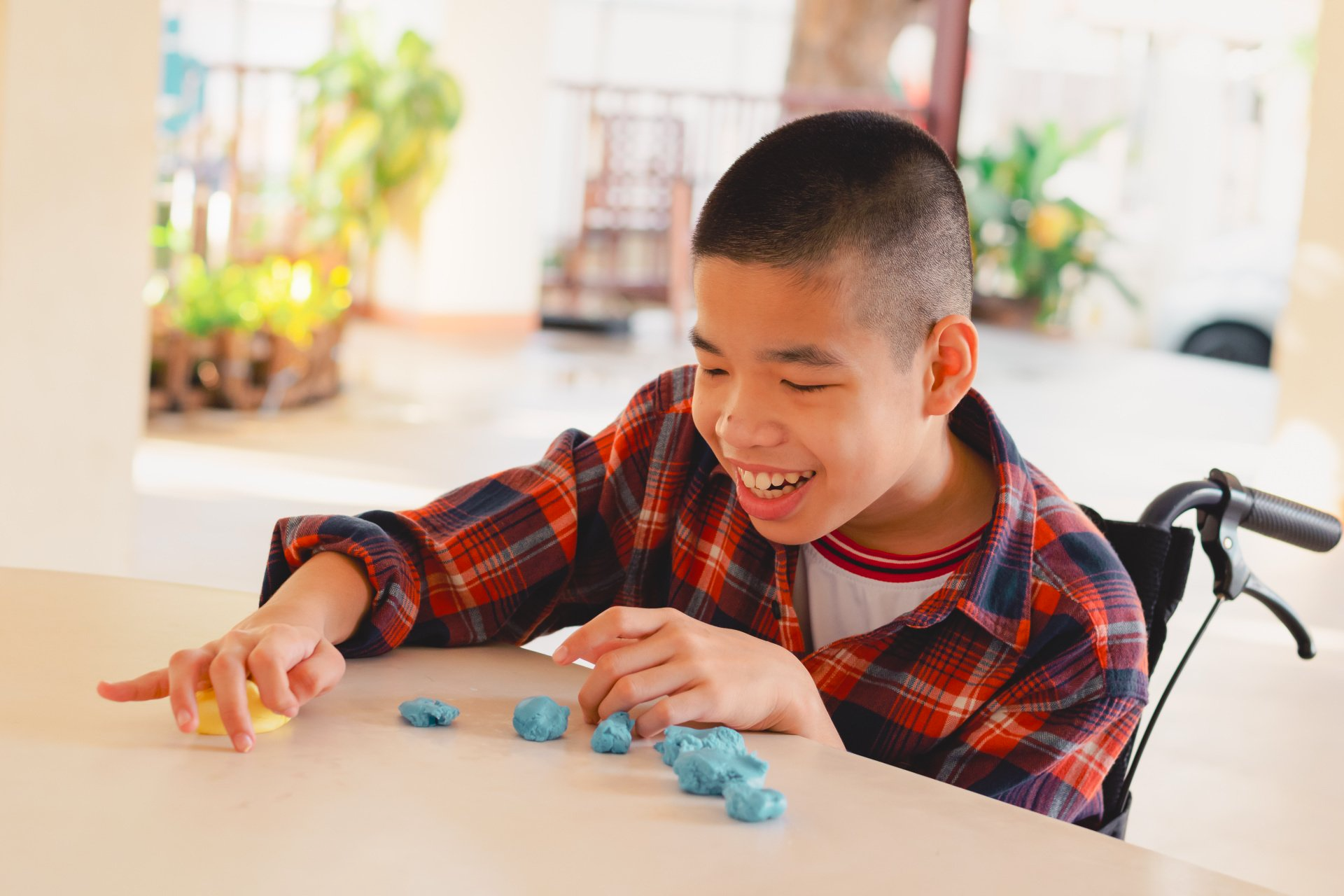A young boy in a wheelchair is playing with blue play dough.