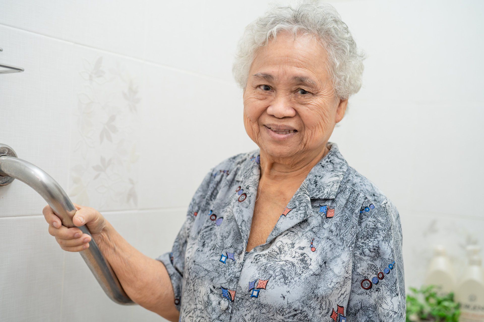 An elderly woman is holding onto a railing in a bathroom.